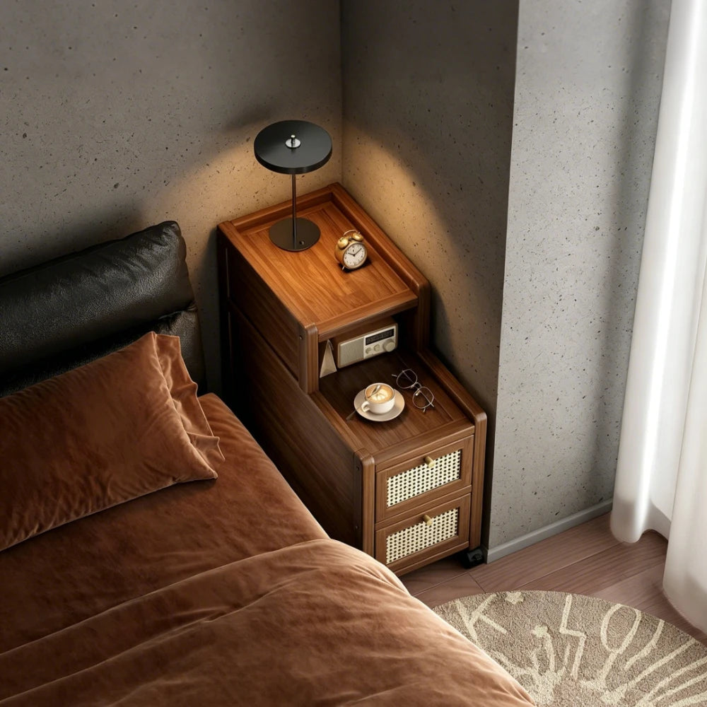 Narrow walnut tone bedside table with cane drawers beside a bed