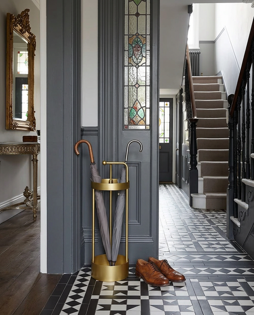 Slim metal umbrella stand by the front door of a Victorian tiled hallway